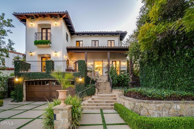 mediterranean / spanish home featuring a garage, stucco siding, a balcony, driveway, and stairs