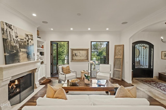 living room featuring baseboards, arched walkways, a fireplace, crown molding, and recessed lighting