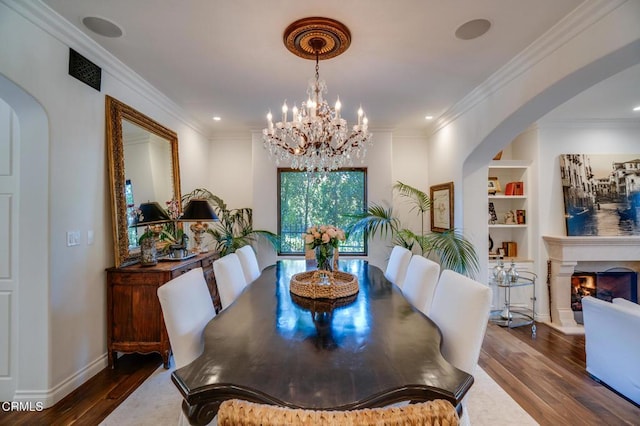 dining room featuring ornamental molding, a chandelier, arched walkways, built in shelves, and wood finished floors