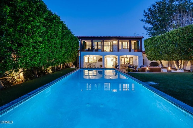 back of property featuring stucco siding, a lawn, a patio area, a fire pit, and an outdoor pool