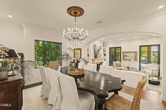 dining area featuring crown molding, arched walkways, a chandelier, and light wood-style floors