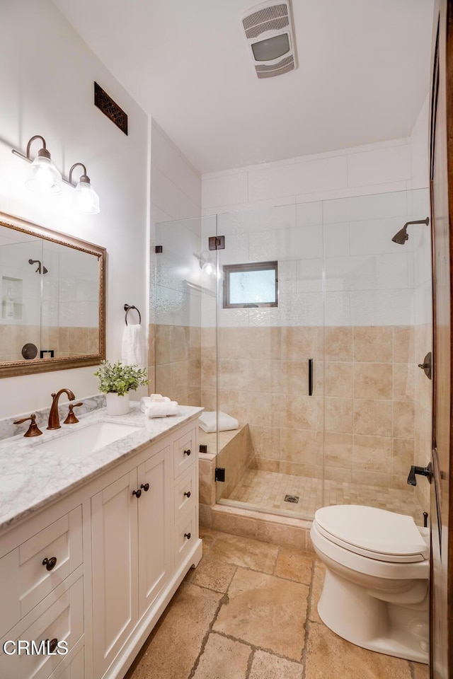 full bath featuring a shower stall, stone tile floors, vanity, visible vents, and toilet