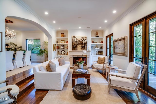 living room featuring crown molding, arched walkways, a notable chandelier, and wood finished floors