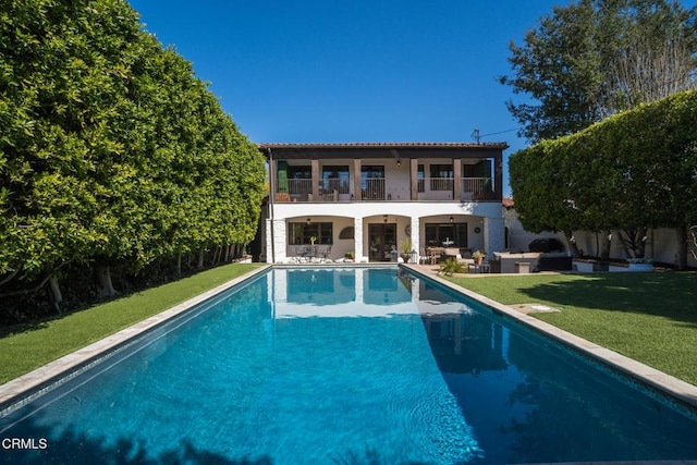 rear view of house featuring a balcony, an outdoor pool, a patio area, a yard, and fence
