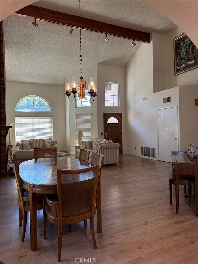 dining area featuring rail lighting, visible vents, a textured ceiling, wood finished floors, and beamed ceiling