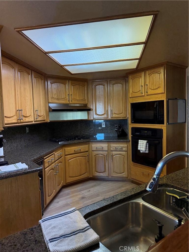 kitchen featuring black appliances, brown cabinetry, a sink, and under cabinet range hood