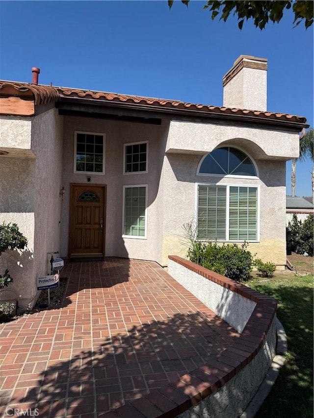 entrance to property with a tiled roof, a patio area, a chimney, and stucco siding