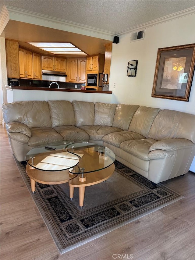 living room featuring light wood-type flooring, a textured ceiling, visible vents, and crown molding