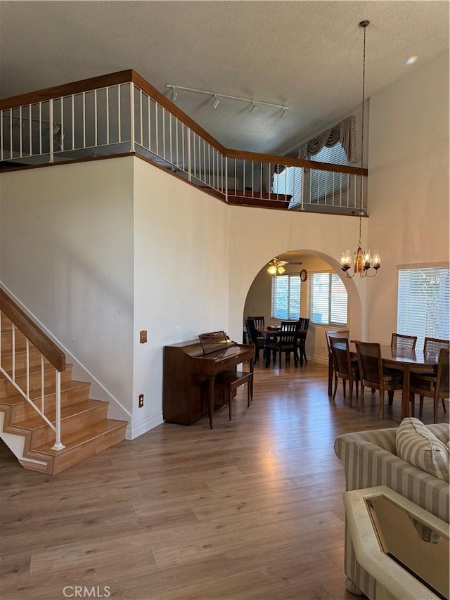 living area with arched walkways, a textured ceiling, wood finished floors, baseboards, and stairs