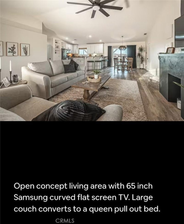 living room with vaulted ceiling, a fireplace, wood finished floors, and a ceiling fan