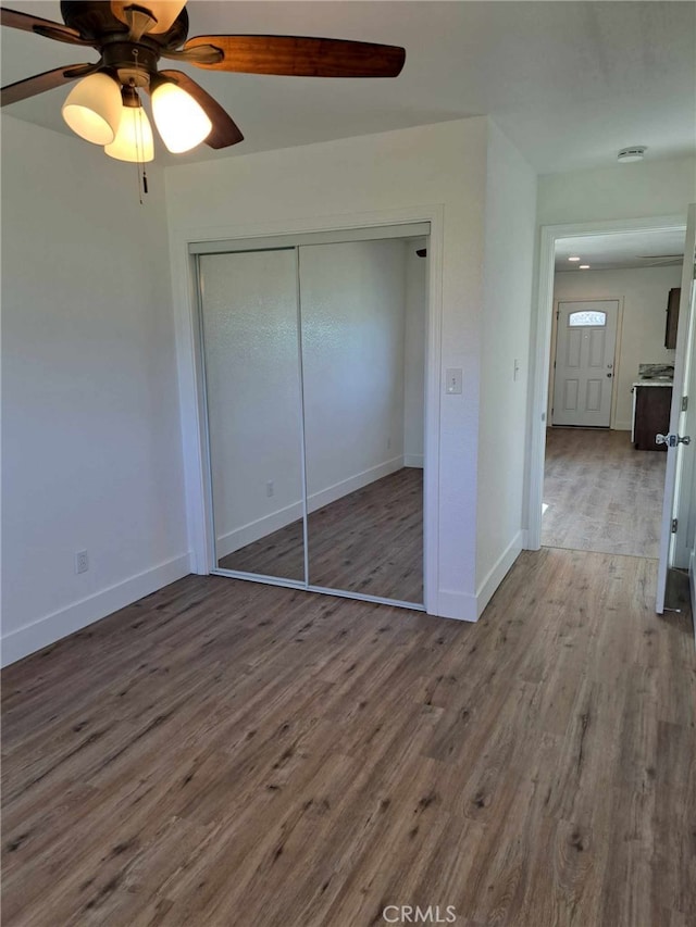 unfurnished bedroom with ceiling fan, a closet, wood finished floors, and baseboards