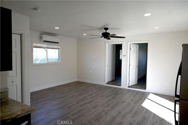 unfurnished bedroom featuring dark wood-style flooring, recessed lighting, freestanding refrigerator, a wall mounted air conditioner, and baseboards