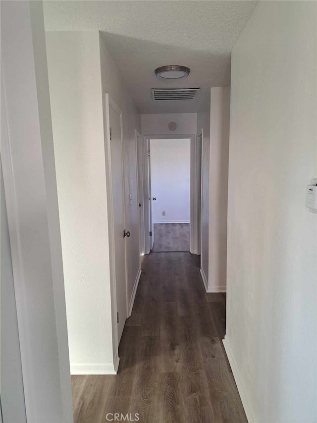 corridor with baseboards, visible vents, dark wood finished floors, and a textured ceiling