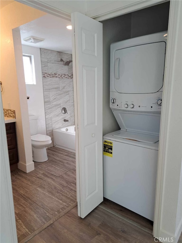 clothes washing area featuring stacked washer and dryer, laundry area, dark wood finished floors, and baseboards