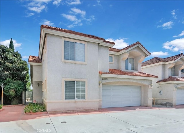 mediterranean / spanish house with a garage, driveway, a tiled roof, and stucco siding