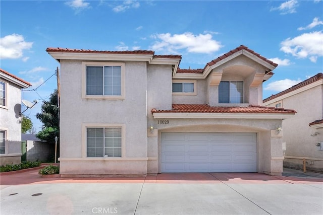 mediterranean / spanish home featuring a garage, concrete driveway, a tiled roof, and stucco siding