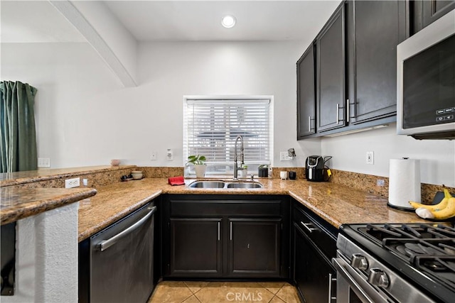 kitchen featuring light tile patterned floors, a sink, appliances with stainless steel finishes, dark cabinetry, and light stone countertops