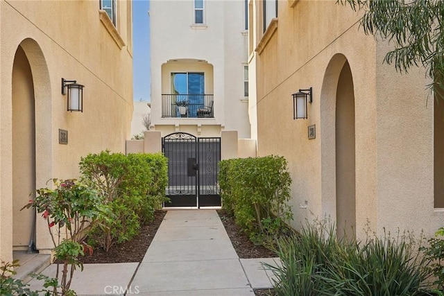 view of exterior entry with a balcony, a gate, and stucco siding