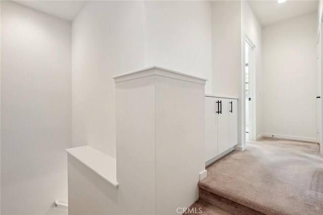 hallway featuring light carpet and baseboards