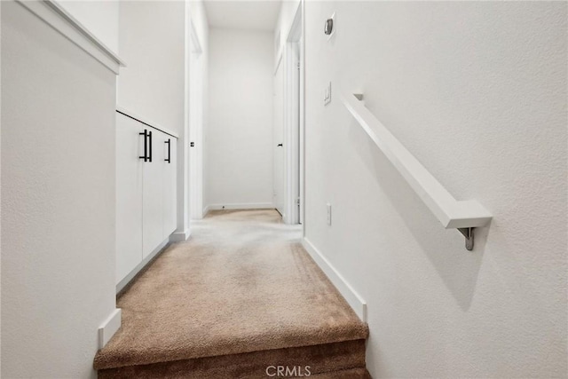 hallway with baseboards and light colored carpet