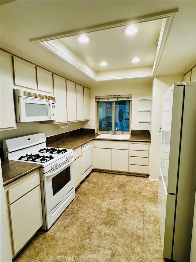 kitchen featuring dark countertops, white appliances, and a raised ceiling