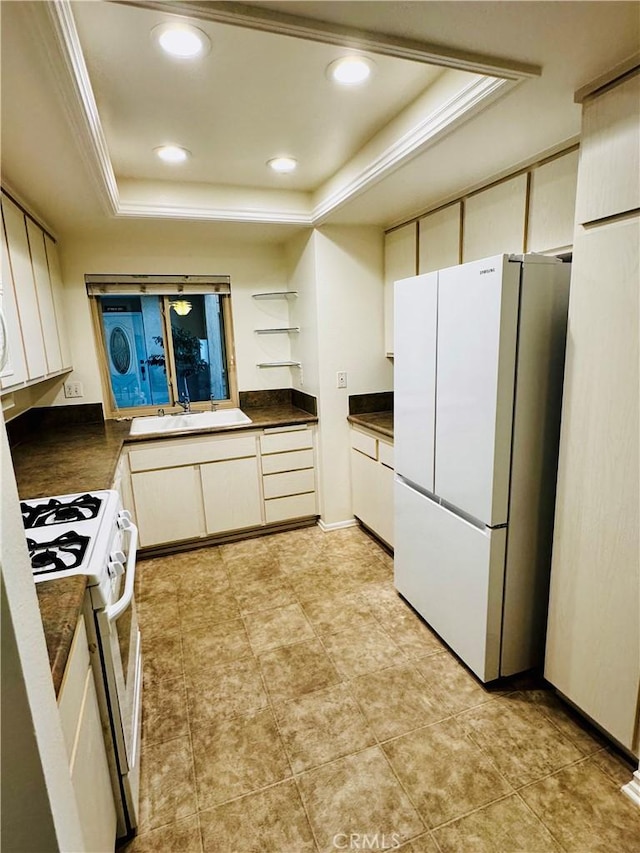 kitchen featuring white appliances, a raised ceiling, dark countertops, open shelves, and a sink