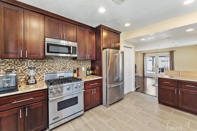 kitchen featuring tasteful backsplash, light stone counters, premium appliances, and french doors