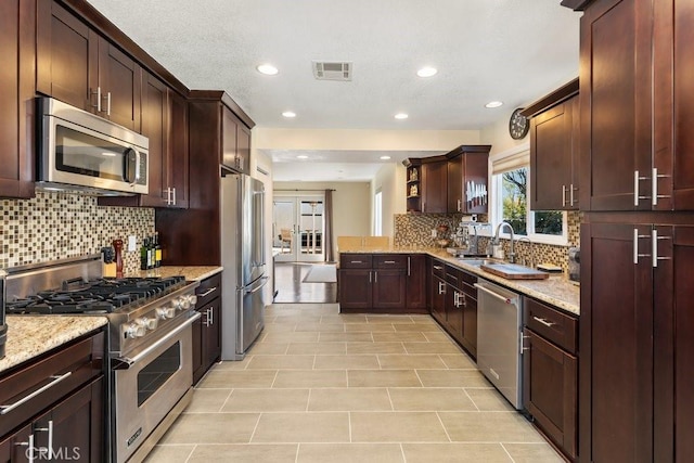 kitchen featuring visible vents, decorative backsplash, appliances with stainless steel finishes, light stone counters, and a sink