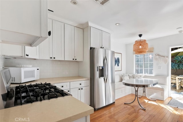 kitchen with stainless steel fridge with ice dispenser, white microwave, decorative light fixtures, light countertops, and white cabinetry