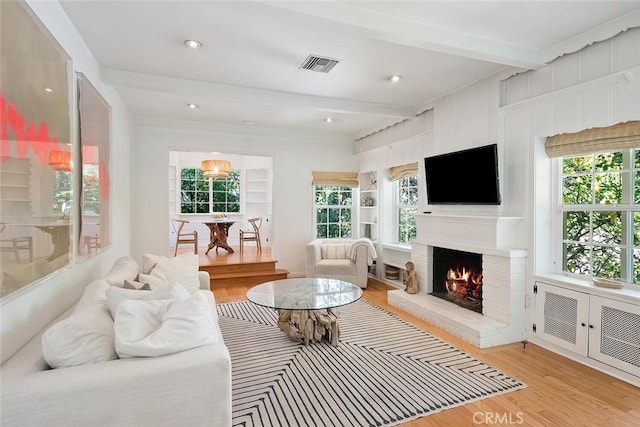 living room featuring plenty of natural light, visible vents, beamed ceiling, and light wood-style flooring