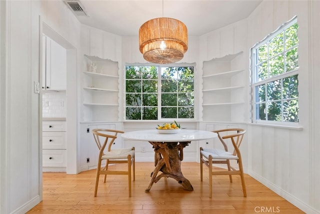 dining room featuring light wood finished floors, breakfast area, visible vents, a decorative wall, and an inviting chandelier