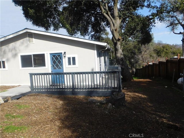 back of house featuring fence, a deck, and stucco siding