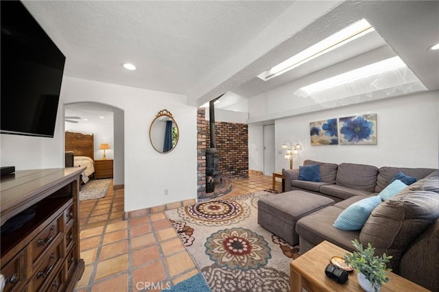 living room featuring arched walkways, light tile patterned floors, recessed lighting, a wood stove, and baseboards