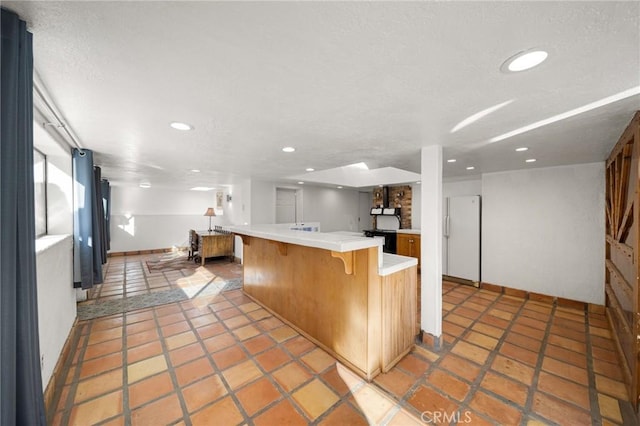 kitchen with recessed lighting, baseboards, freestanding refrigerator, brown cabinets, and a kitchen bar