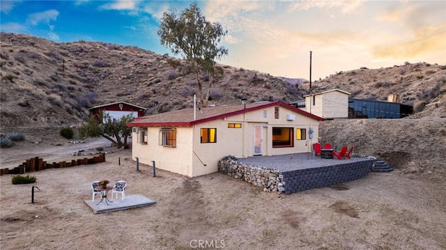back of property at dusk featuring a patio, a mountain view, fence, and stucco siding