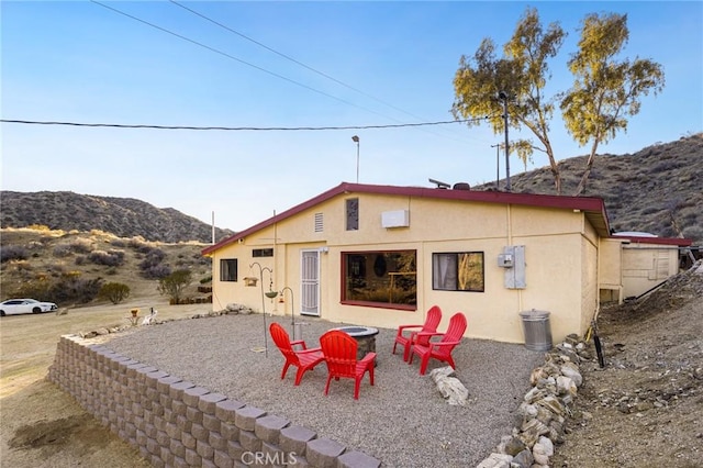 back of house featuring a fire pit, a mountain view, and stucco siding