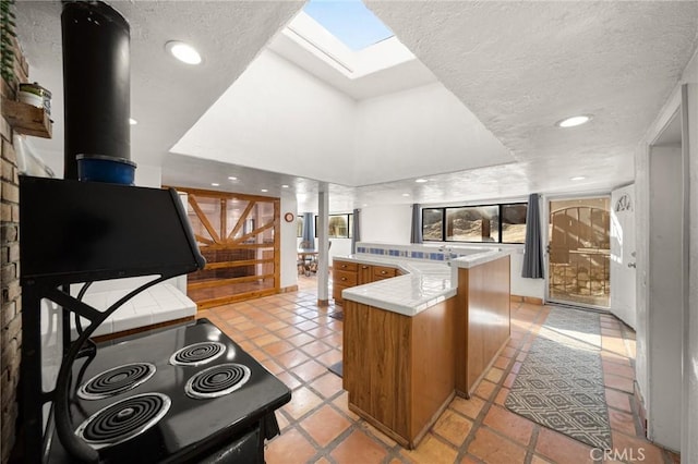 kitchen with a skylight, tile counters, brown cabinetry, a peninsula, and a textured ceiling