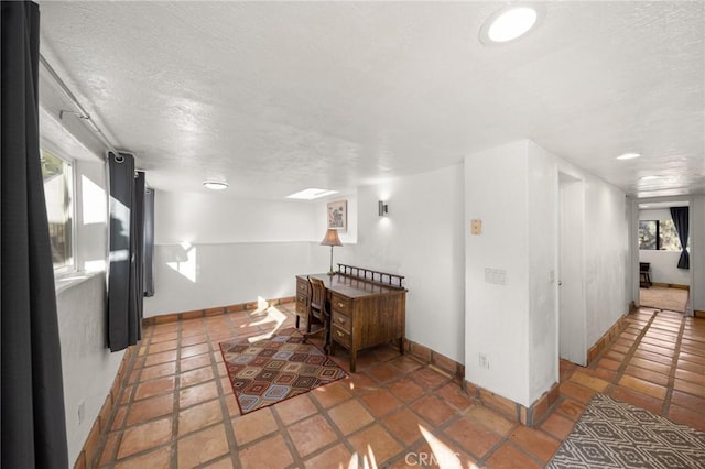 interior space with a skylight, baseboards, and a textured ceiling