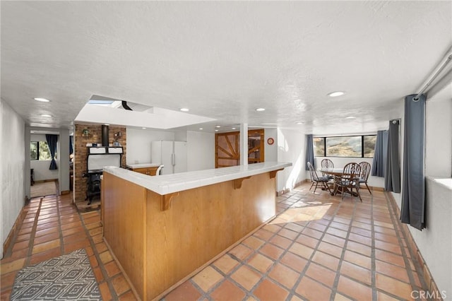 kitchen with a textured ceiling, plenty of natural light, freestanding refrigerator, and a kitchen breakfast bar