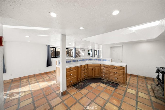 kitchen featuring recessed lighting, light countertops, a wood stove, a textured ceiling, and a peninsula