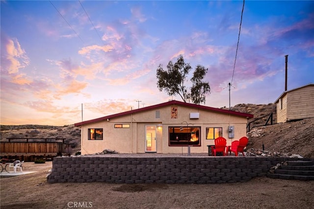back of house at dusk with stucco siding, fence, a patio, and an outdoor fire pit
