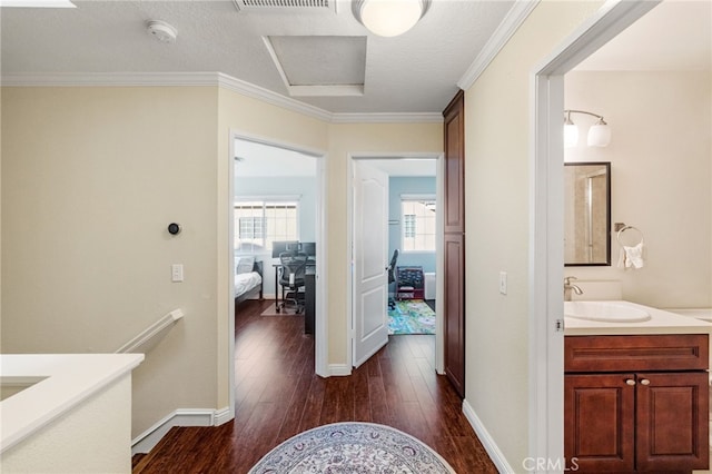 hall with dark wood-type flooring, crown molding, a sink, and baseboards