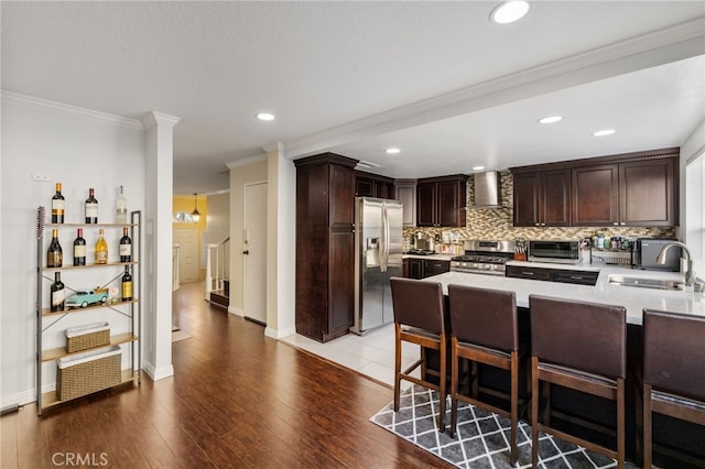 kitchen with stainless steel appliances, light countertops, a sink, a peninsula, and wall chimney exhaust hood