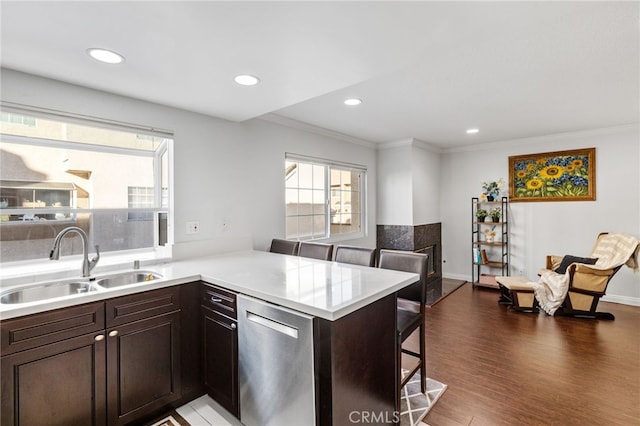 kitchen with light countertops, a sink, dishwasher, a peninsula, and a kitchen bar