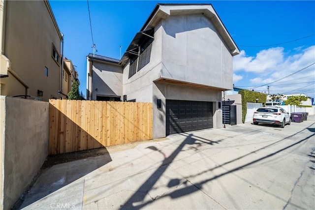 view of side of property with fence, driveway, an attached garage, and stucco siding