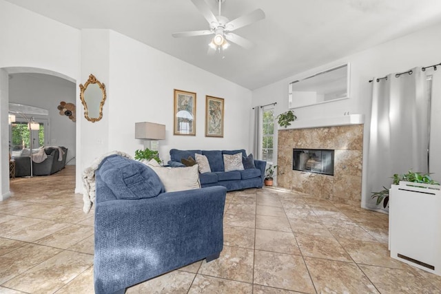 living room with arched walkways, a tiled fireplace, lofted ceiling, ceiling fan, and tile patterned floors