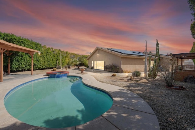 pool at dusk with a patio area, a pool with connected hot tub, and a pergola