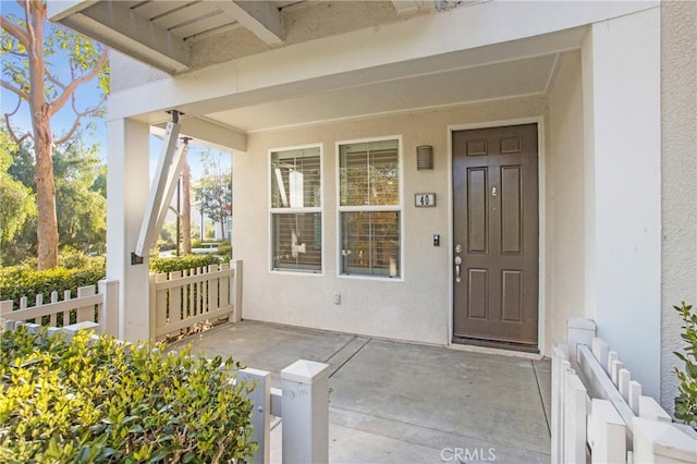 doorway to property with a porch, fence, and stucco siding