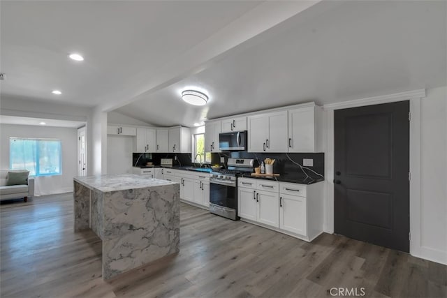 kitchen featuring vaulted ceiling with beams, stainless steel appliances, a sink, and wood finished floors