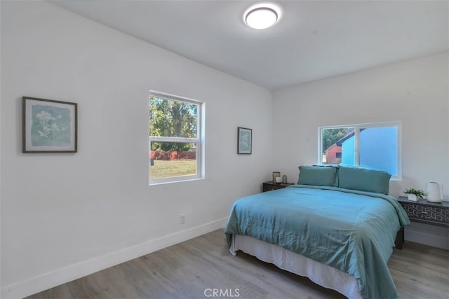 bedroom featuring multiple windows, baseboards, and wood finished floors